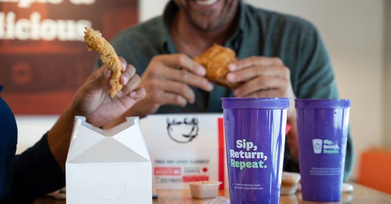 People eating chicken, purple cups in the foreground