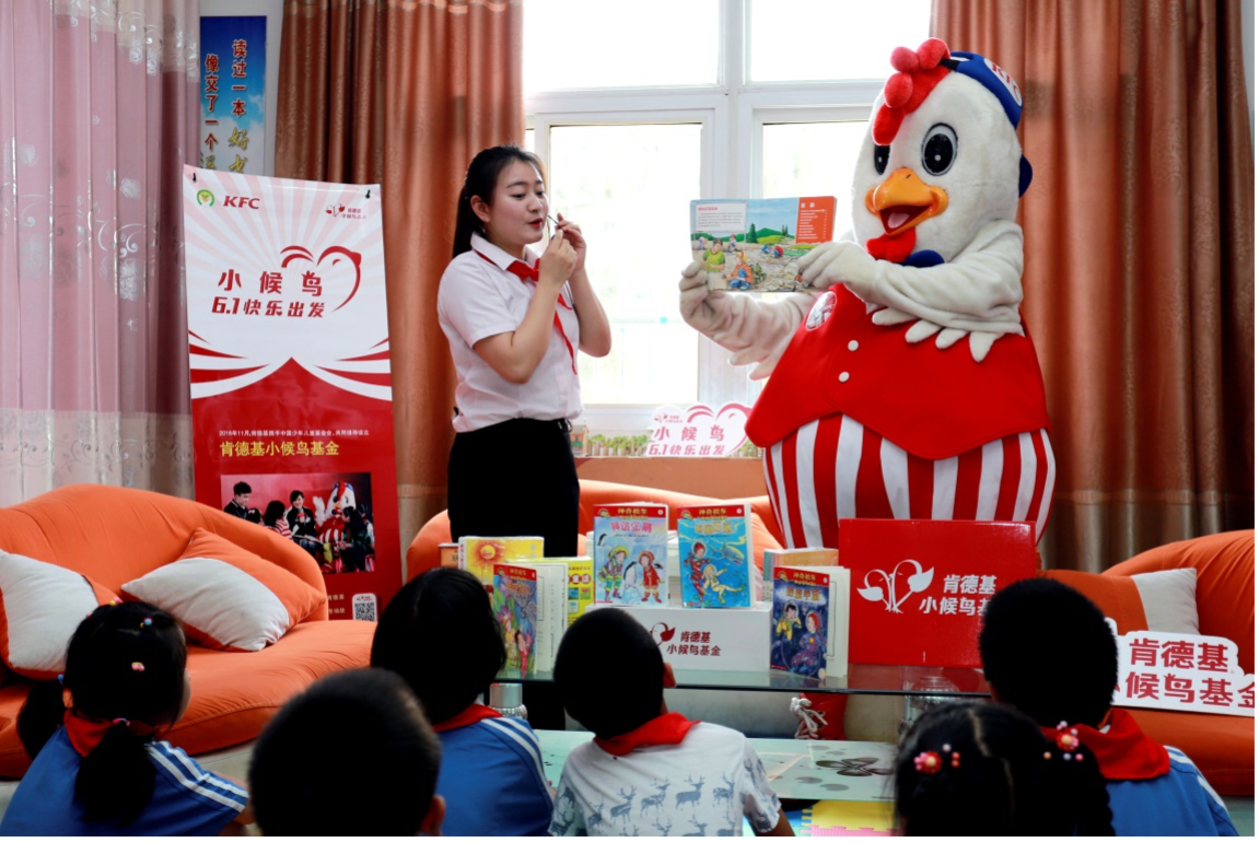 person in chicken costume reading to group of kids