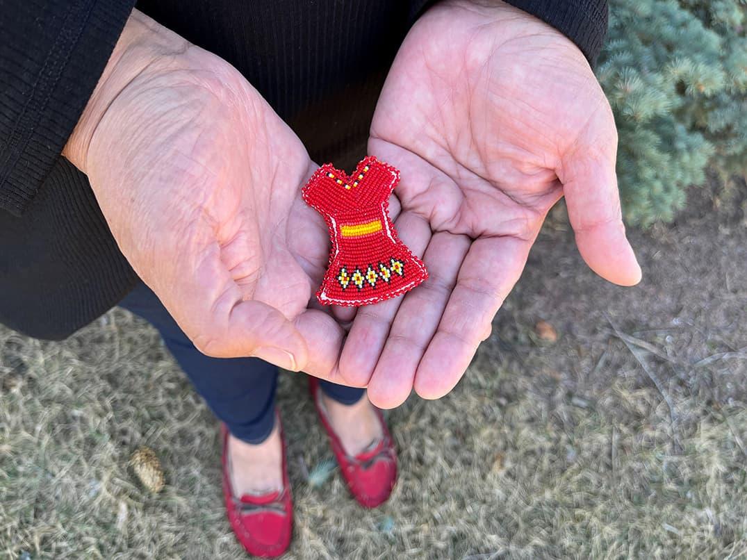 Hands holding a miniature red dress made of beads