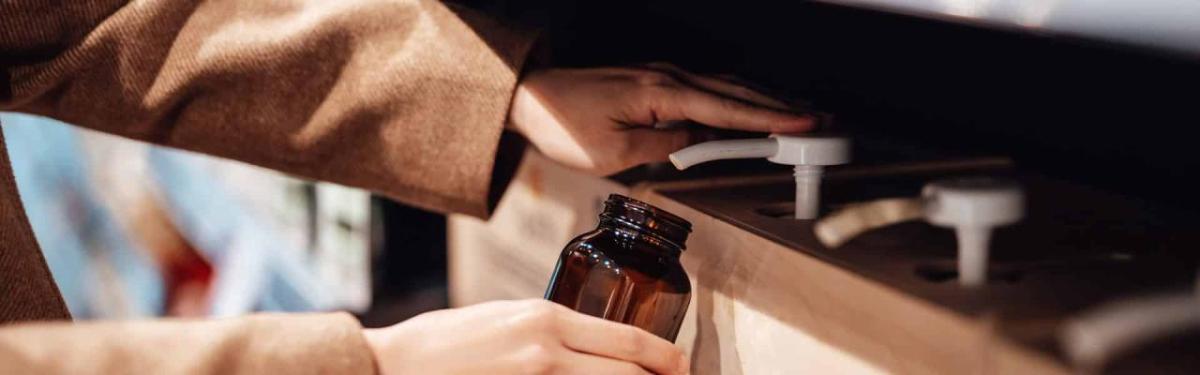 A person filling a brown glass jar from a row of pumps.