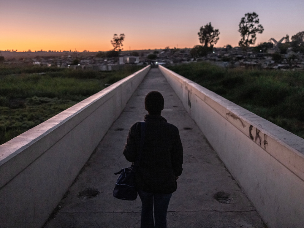 A silhouette of a person walking a narrow path towards houses in twilight.