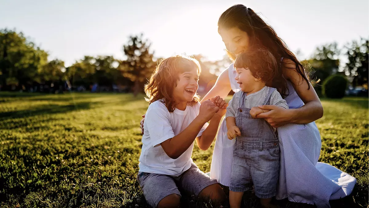 An adult and two children laughing, in an outdoor setting.