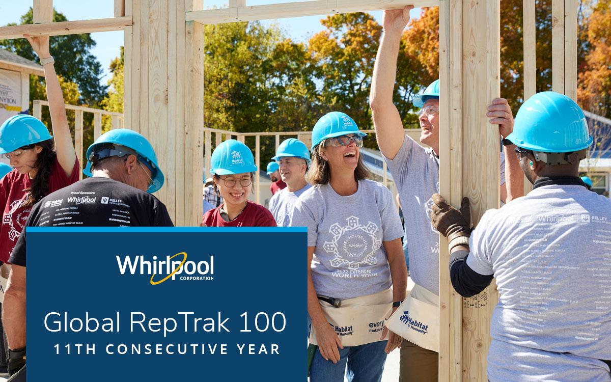 A group of people in matching blue hard hats, some holding wood framing on a construction site.