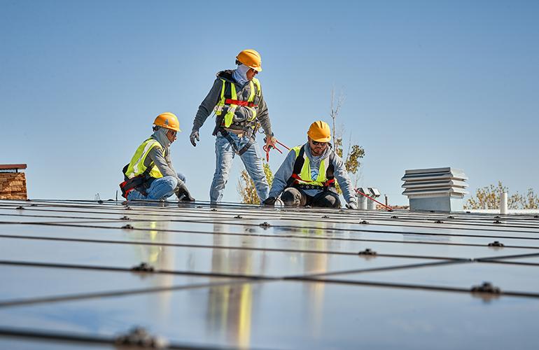Credit: Sunnova Three people in high-vis garments and hard hats installing solar panels.