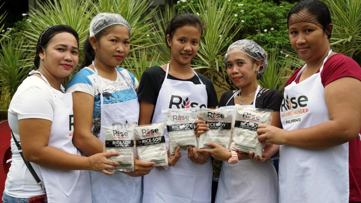 Volunteers posed with bags of food. "Rise against Hunger" on their aprons.