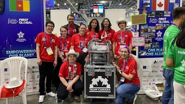 Team in matching shirts next to cases marked "Team Canada" at a robotics event.