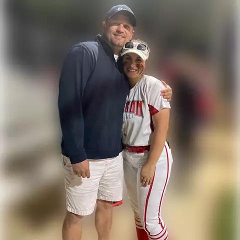 Two people posed, hugging. One in a baseball uniform.