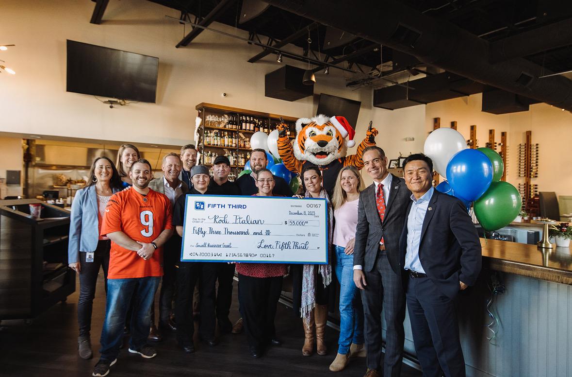 A group posed in a restaurant with a large check. A tiger mascot behind them.
