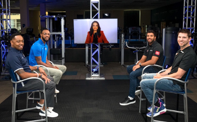 a group of four people an a person appearing on a monitor all seated in a studio