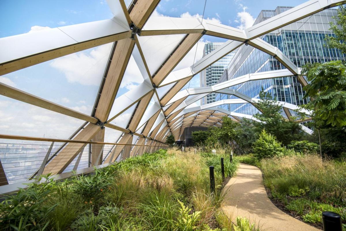 A walkway through lush greenery, a glass curved ceiling overhead.