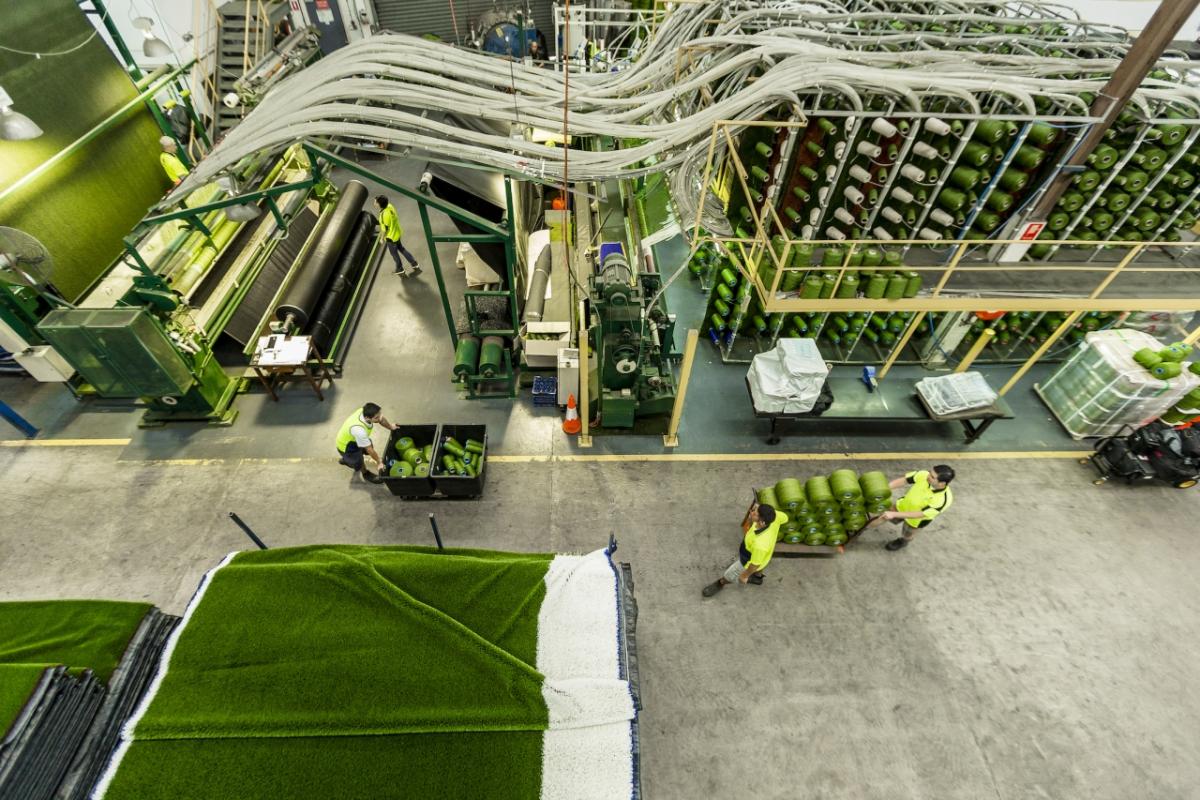 factory workers in safety gear stack and move bins of green plastic