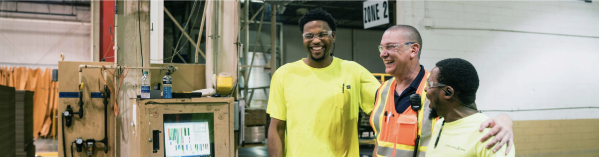 workers in safety gear with arms on each others' shoulders and laughing