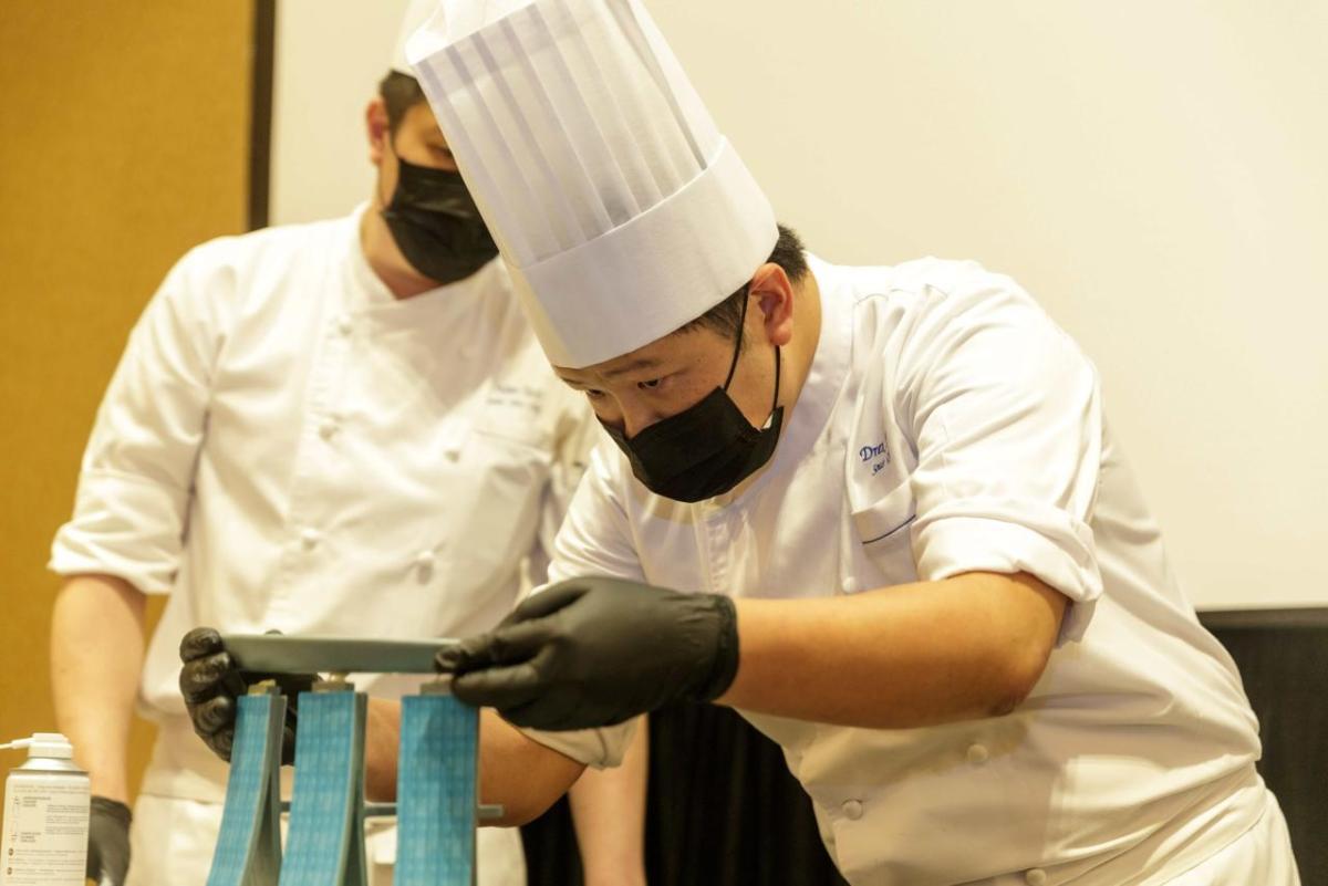 student in a chef's uniform carefully balancing a plate