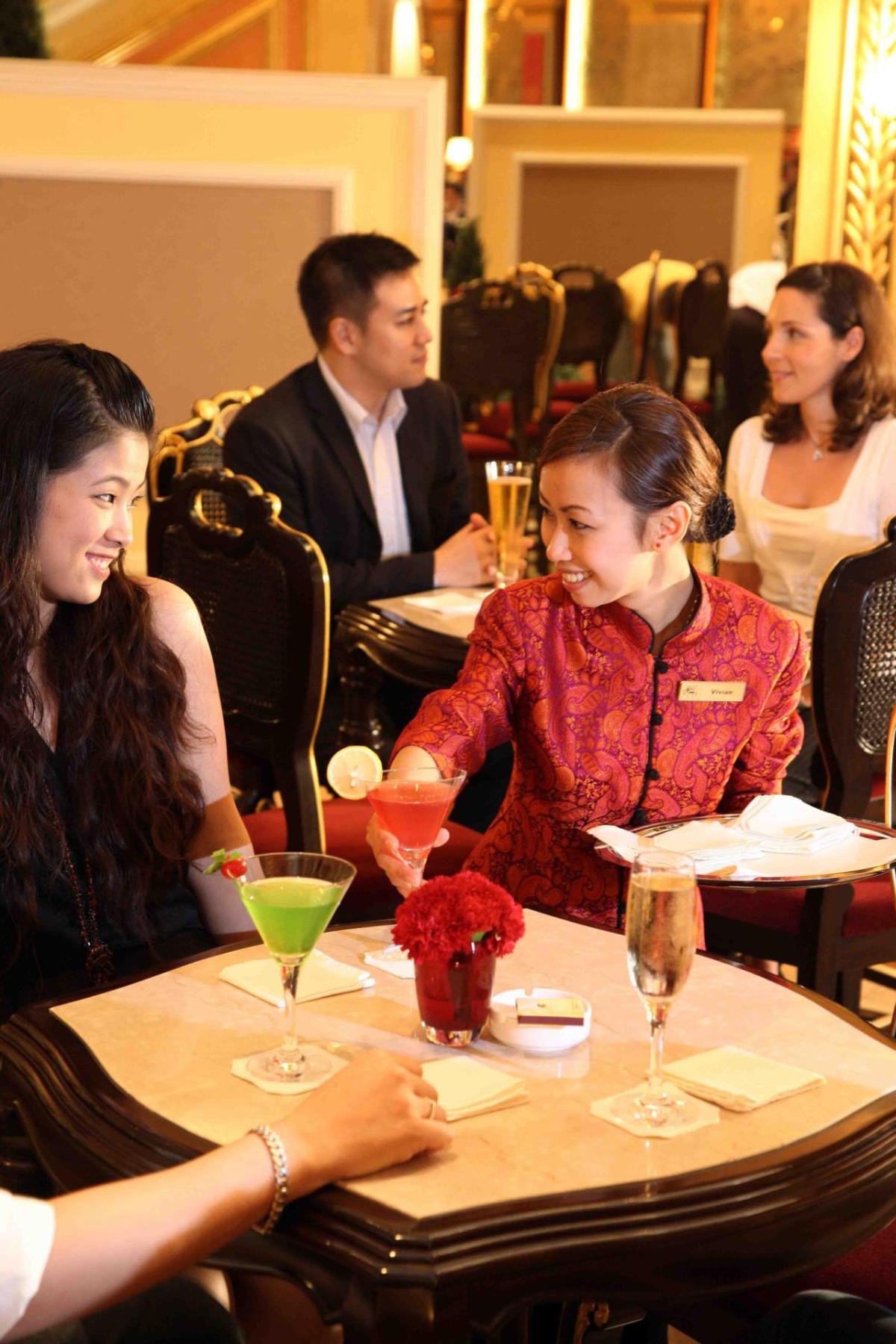 student in a red jacket places colorful cocktails on a small table