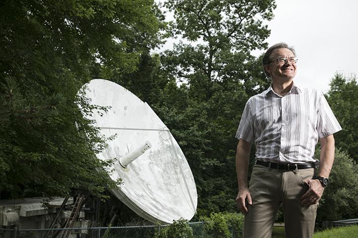 George Mason University associate professor Peter Pachowicz said the salvaged satellite dish gives Mason students the chance to "join the renewed space race." Photo by Ron AIra. A person standing outside looking to the sky, a large satellite dish behind them