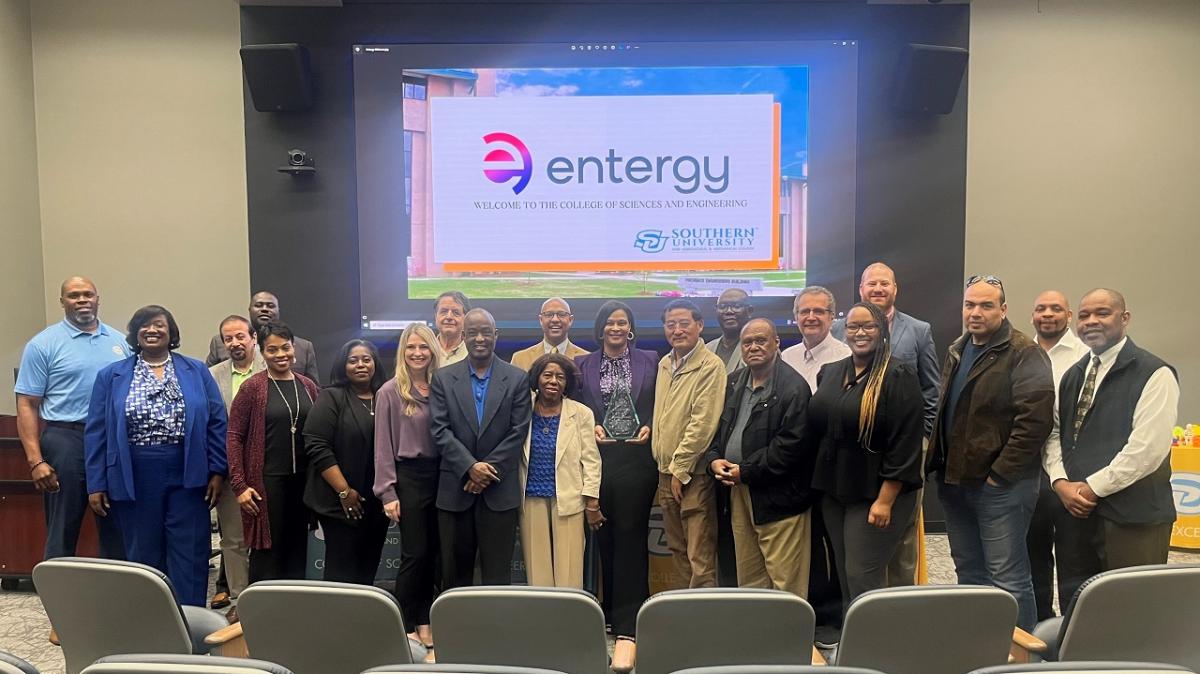 A group of people posed at the front of an auditorium. A digital display behind them with the entergy logo showing.