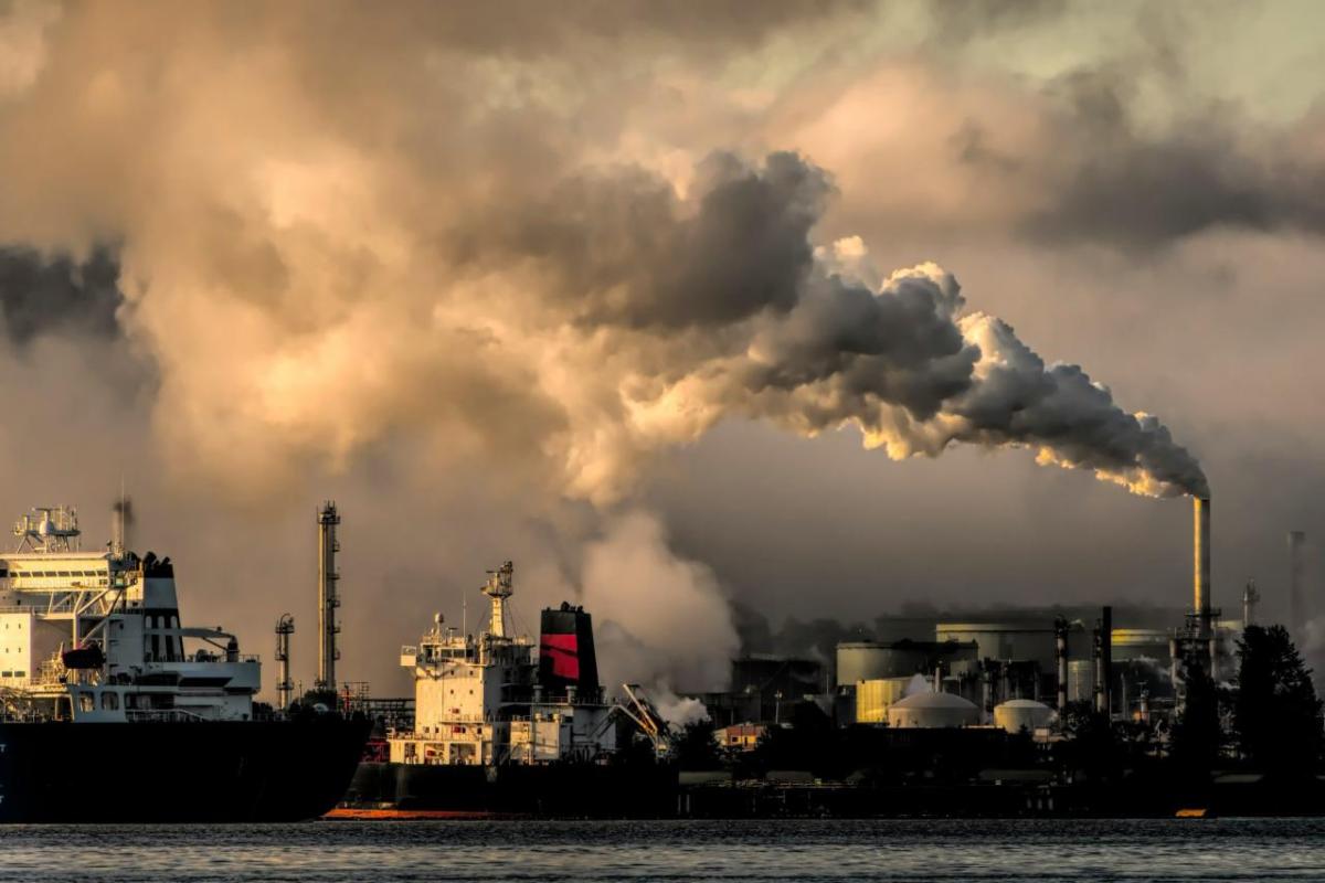 Smoke stacks with billowing clouds and a cloud covered sky behind.