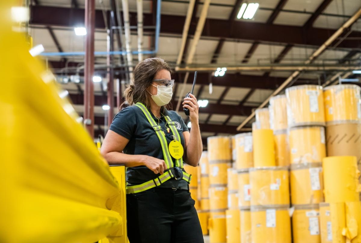 Karen Crisp has spent 23 years in the manufacturing industry. Karen Crisp in safety gear standing among yellow barrels in a factory
