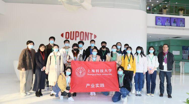 a group of people standing in front of a DuPont logo on a wall, holding a red sign with writing in a foreign language