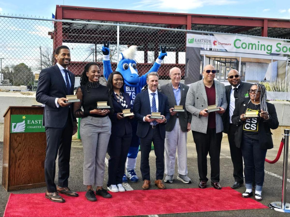 People standing together on a red carpet along with a blue mascot, holding awards