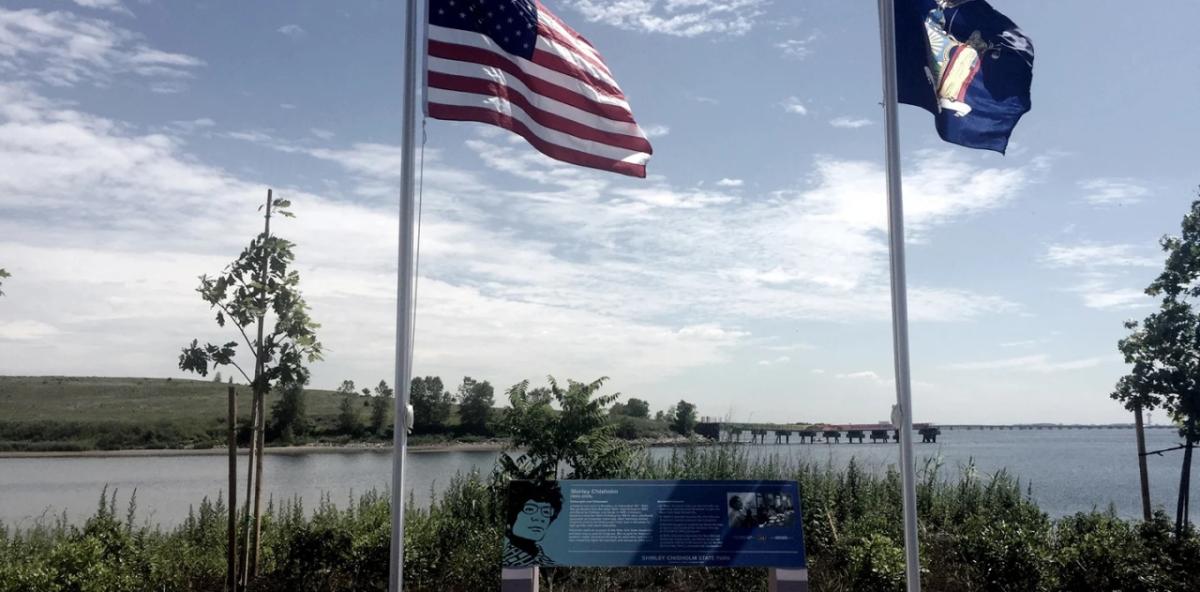 two flags on poles, a water way and peninsula behind them