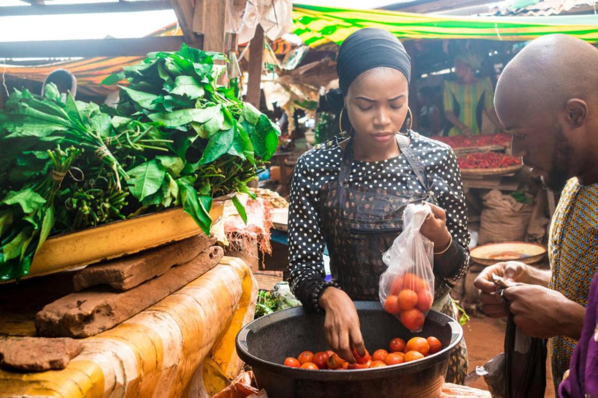 Bayer set the goal to support 100 million smallholder farmers in low- and middle-income countries by 2030. A person bagging produce for another watching on.