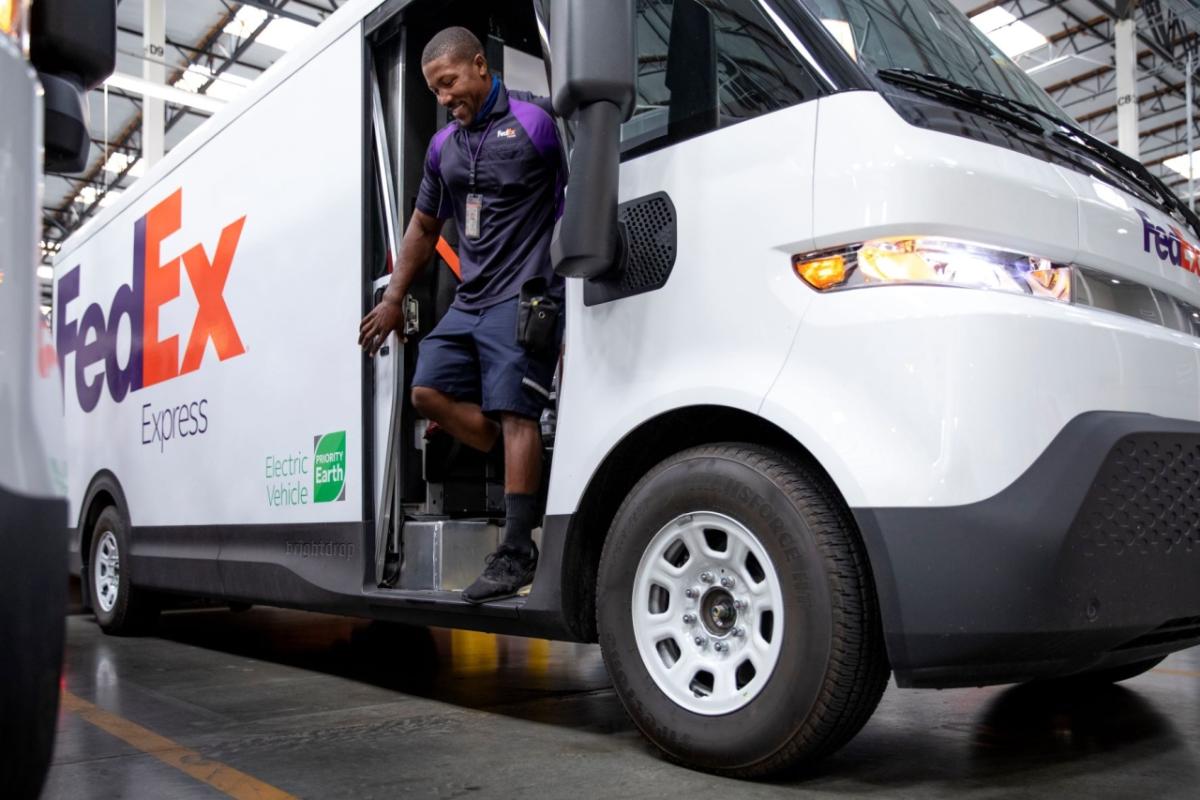 Smiling employee exiting a FedEx electric vehicle