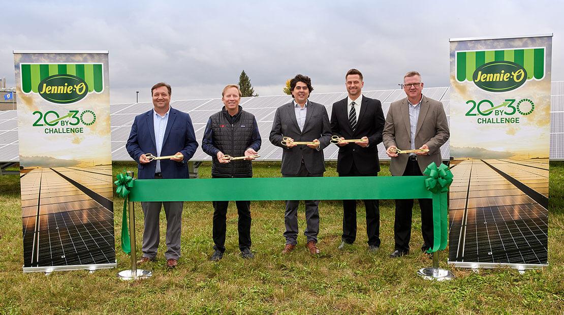 5 executives holding golden scissors behind a green ribbon in front of a solar array