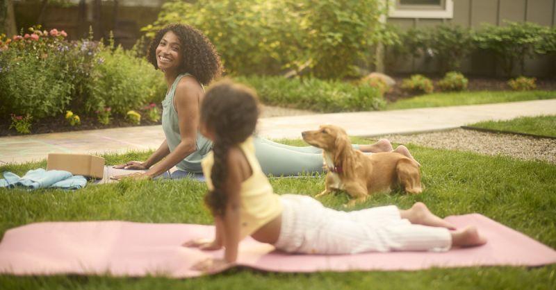 Adult and child doing yoga on a lawn with a dog nearby