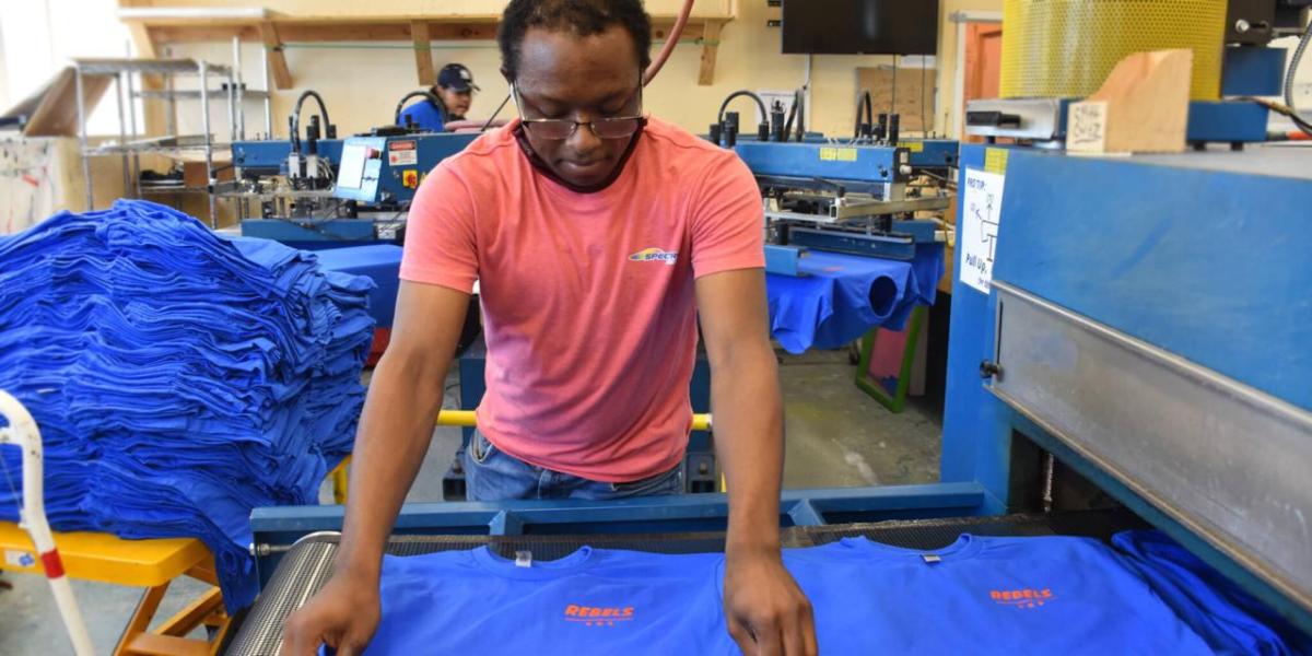 A person lays a t-shirt neatly on a conveyor.