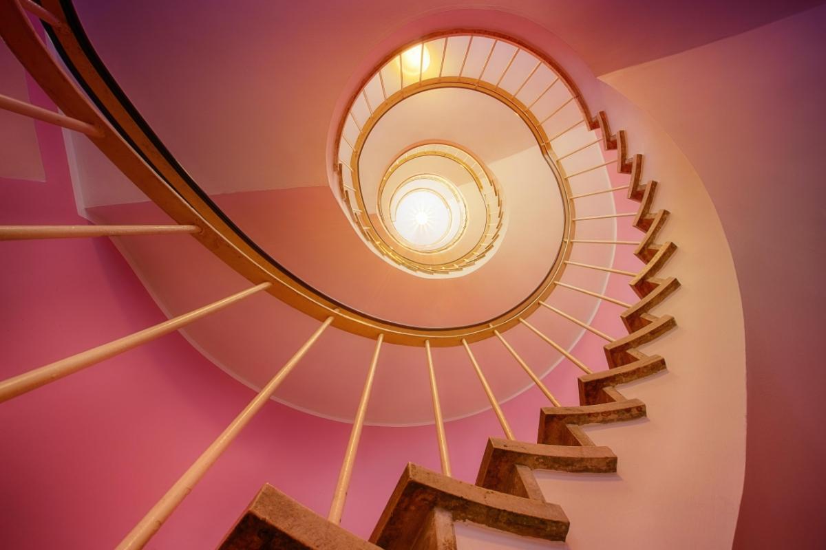 Looking up a long spiral staircase, pink hues on the wall.