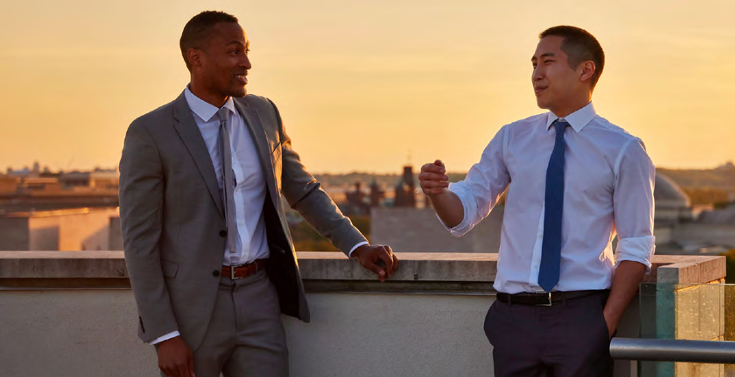 Two people in suits standing on a rooftop talking