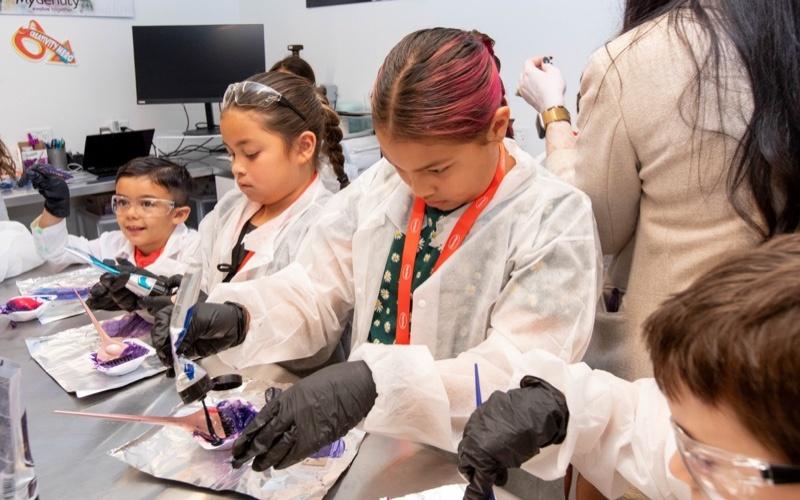 Children in protective lab gear doing experiments at a table.