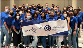 A group in matching blue shirts, masks, gloves. The front row holding a sign "We volunteered at Holy Apostus."