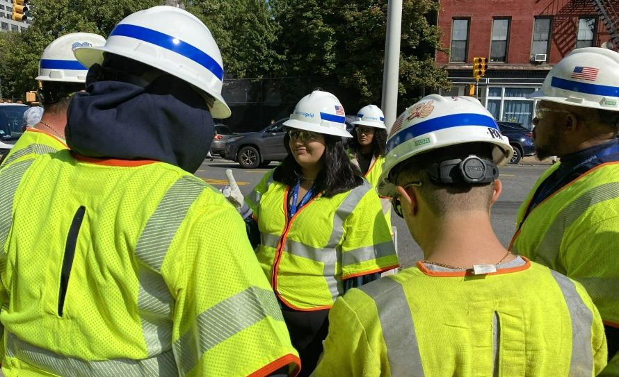 Leela talking to a group of employees. All in high-vis and protective gear outside.