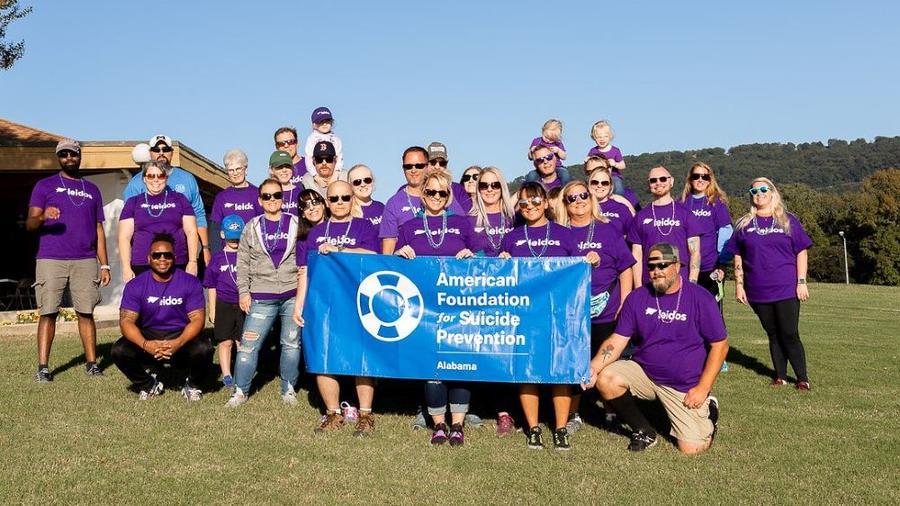 Leidos employees and family members participating in the American Foundation for Suicide Prevention’s Hike for Hope event in Huntsville, Alabama. A group of people in matching shirts outdoors. Some holding a sign "American Foundation for Suicide Prevention."