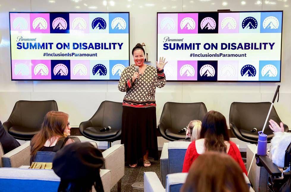 A person with a microphone waving to a group of seated people. "Summit on Disability" signs behind them.