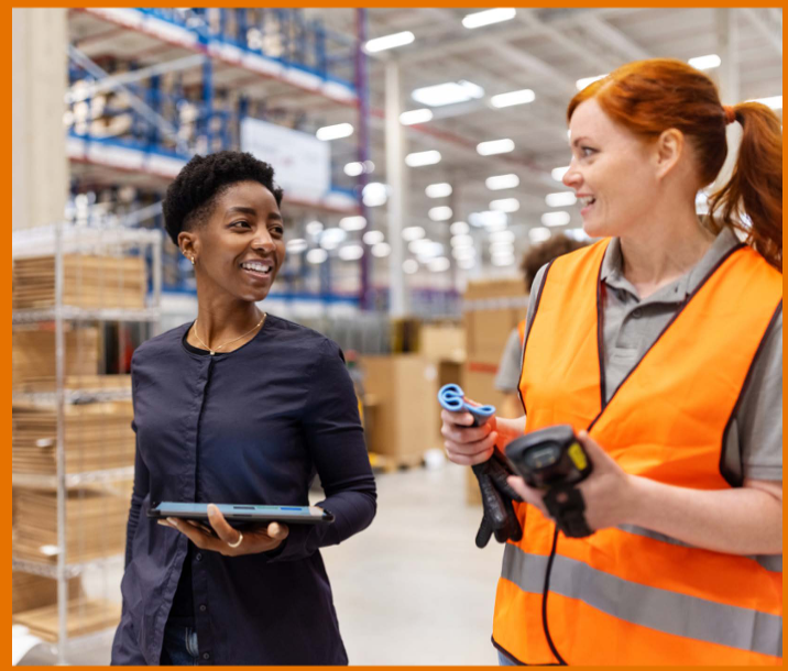 Two people in a warehouse, one wearing an orange vest.