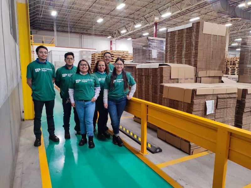 A group of volunteers in matching shirts, a warehouse of paper products behind them.