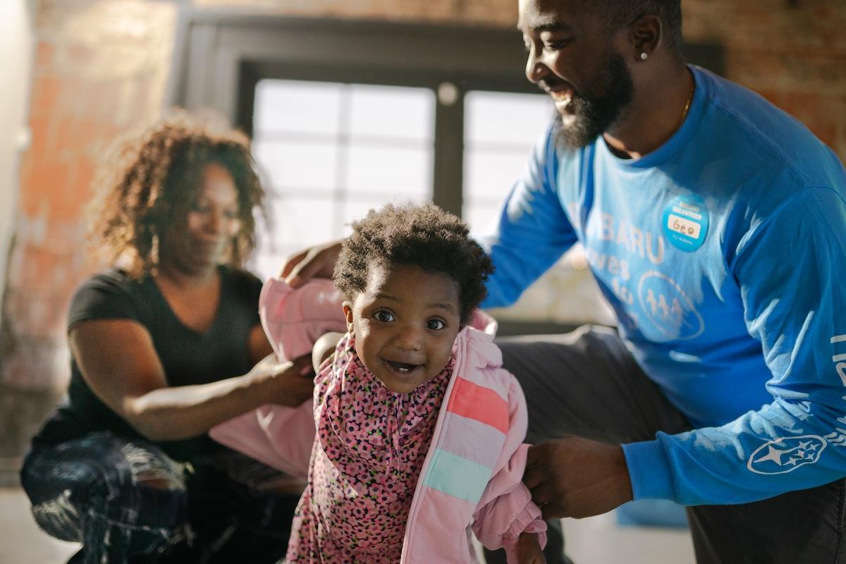 people helping a child put on a coat