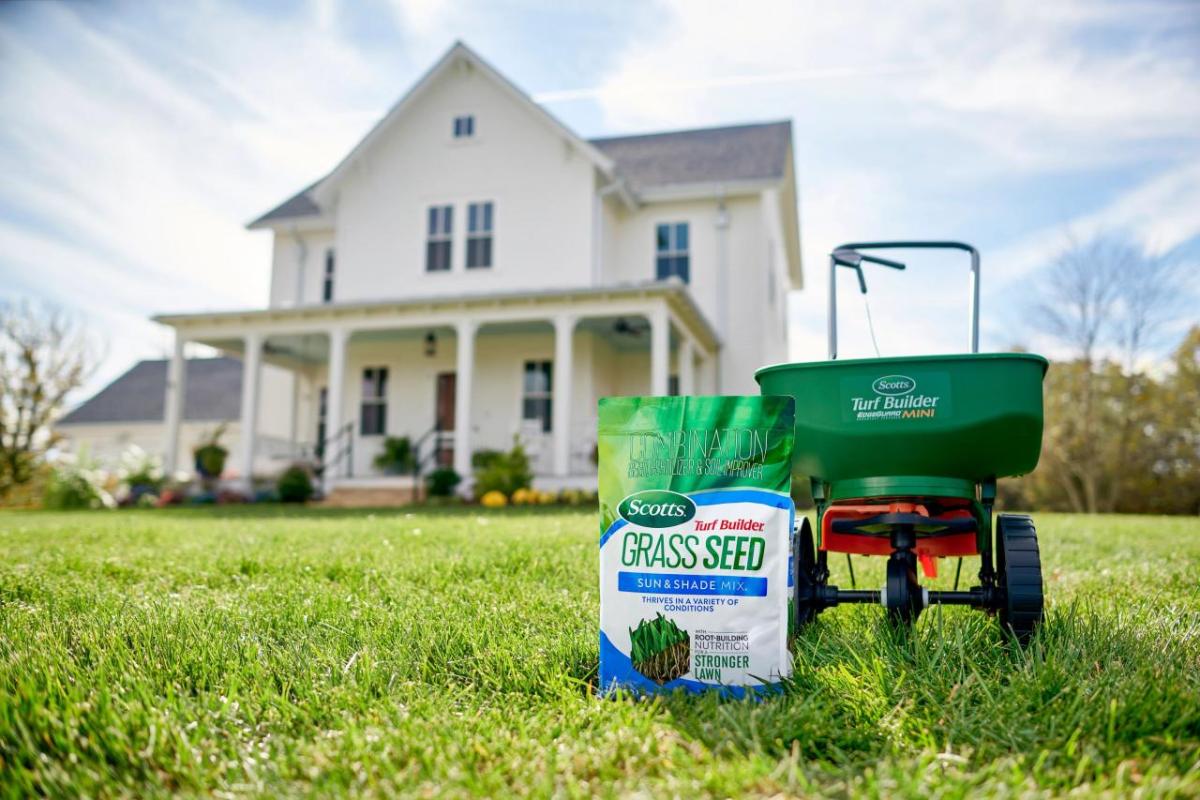 A bag of Scotts Grass Seed next to a spreader, in front of a house