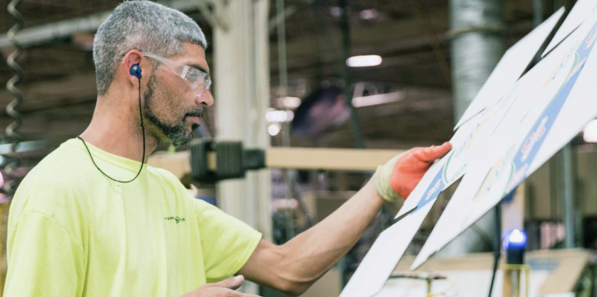 worker in a yellow shirt and orange gloves inspecting a piece of cardboard