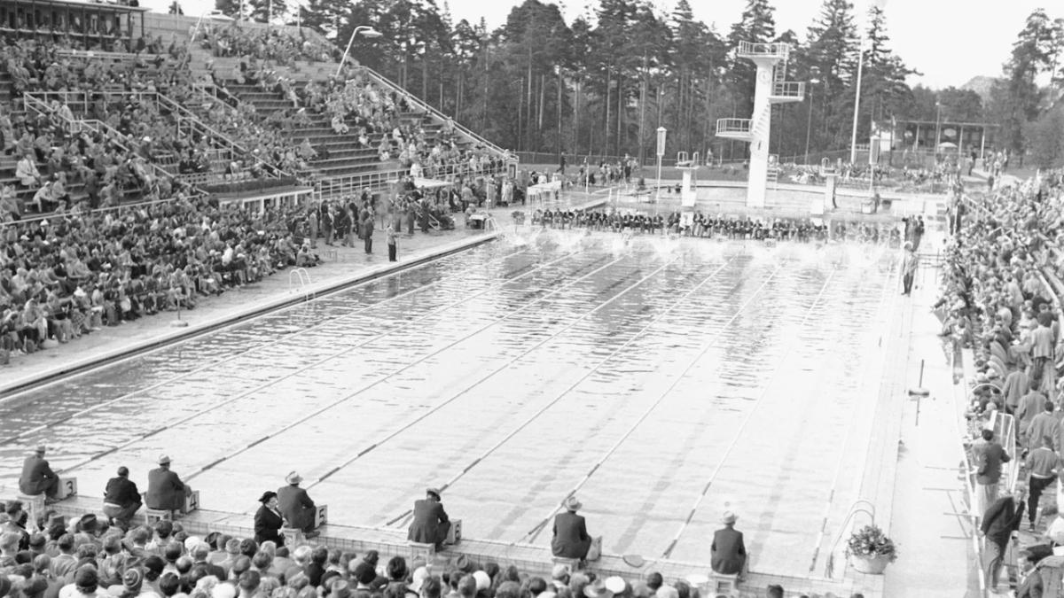 black and white aerial view of a large swimming pool and spectators in filled stands