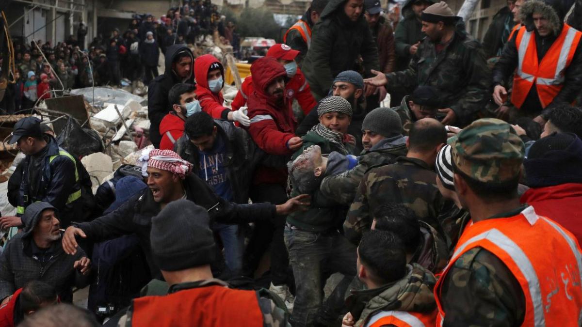 Civil defense workers and security forces carry an earthquake victim as they search through the wreckage of collapsed buildings in Hama, Syria