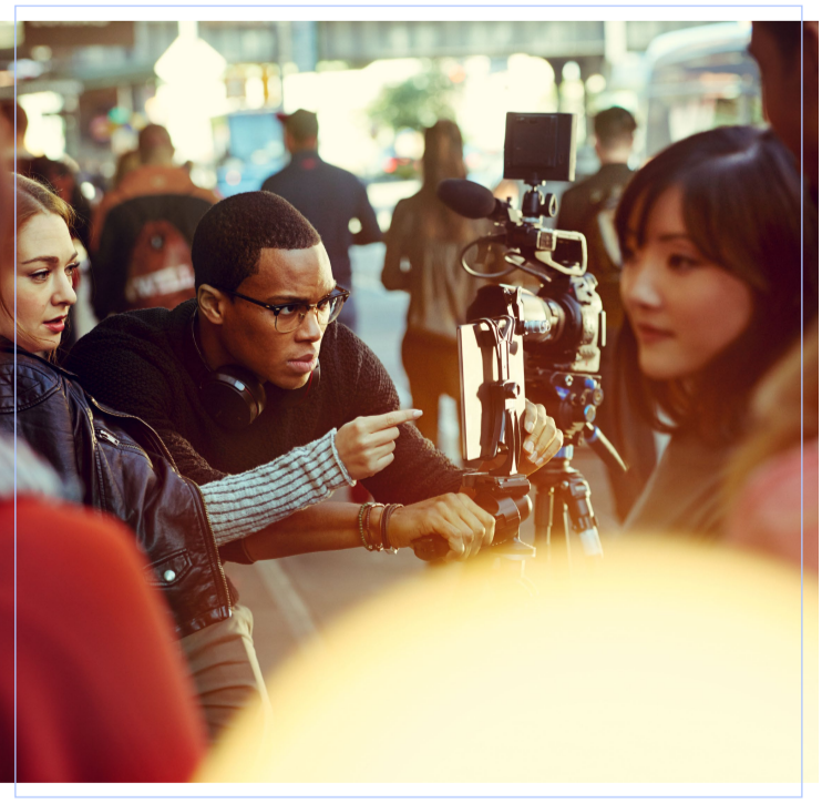 A group of people, some blurred in the background. Some looking at a movie camera