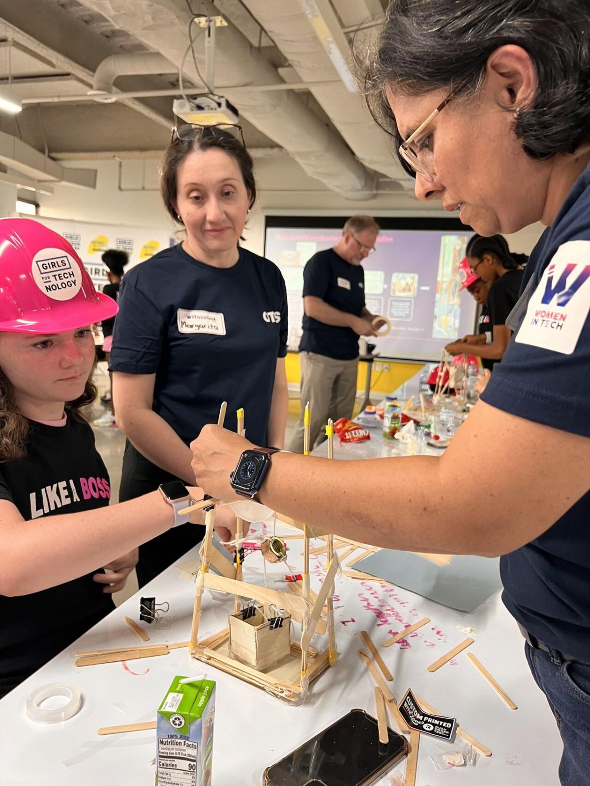 Adult volunteers and children working on building model structures with craft supplies.