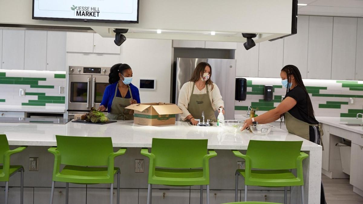 three people in aprons and masks in a large kitchen