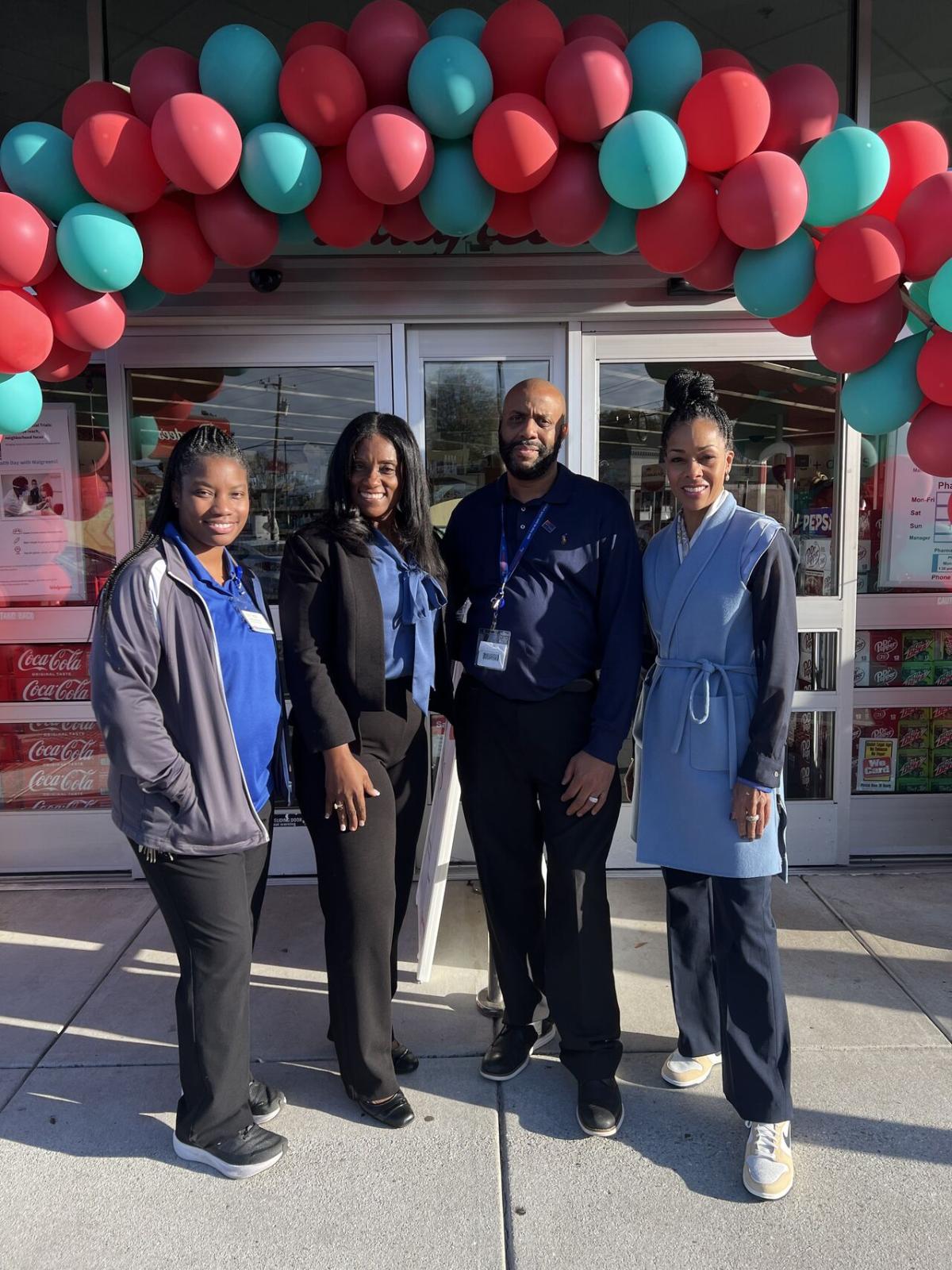 Four people posed outside a Walgreens. A balloon arch over the entrance.