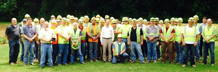 A large team of people posed in a group. Most wearing high-vis vests and safety hats.