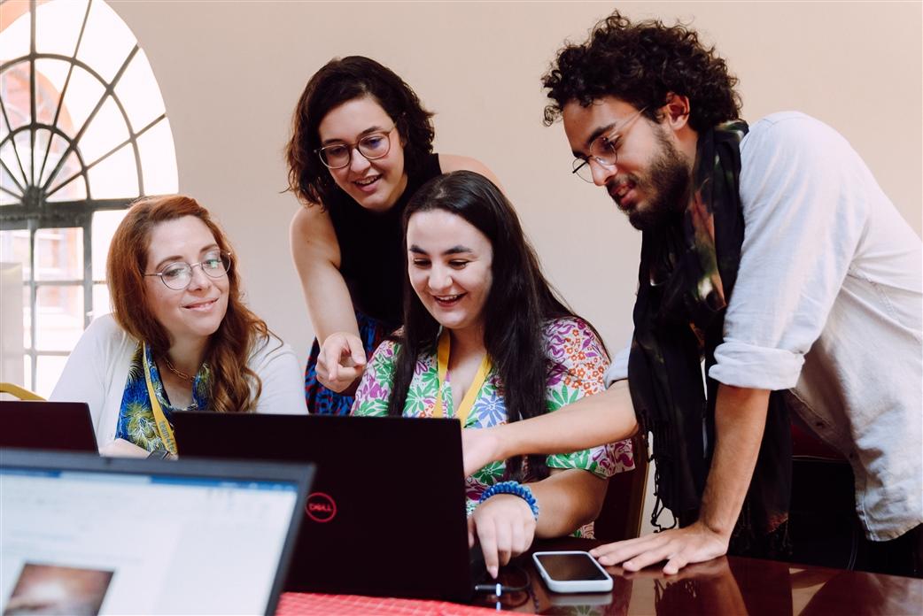 Four people at a desk looking at the same laptop